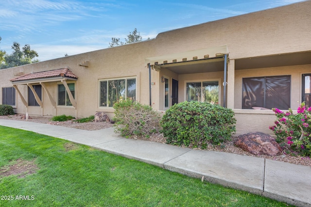 rear view of house with a tile roof, stucco siding, and a yard