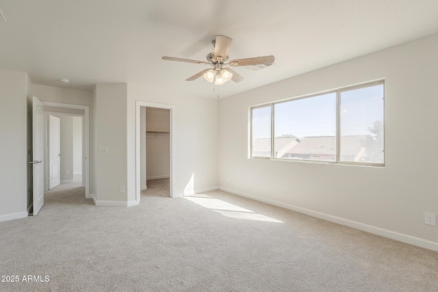 unfurnished bedroom with light carpet, a closet, a walk in closet, and baseboards