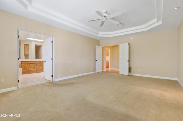 unfurnished bedroom with connected bathroom, ceiling fan, a raised ceiling, and light colored carpet