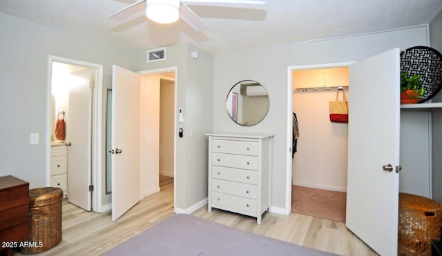 bedroom with a walk in closet, ceiling fan, visible vents, light wood-type flooring, and baseboards
