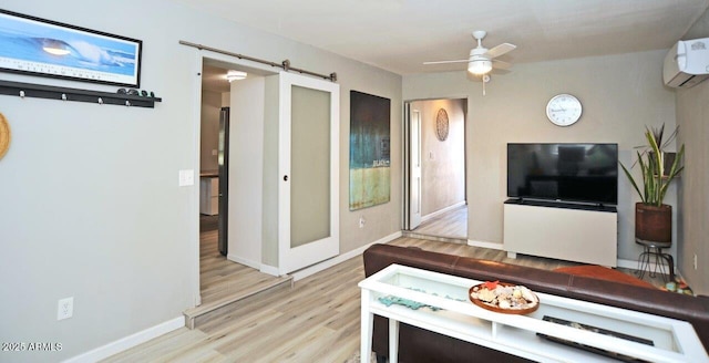living area with ceiling fan, a barn door, a wall mounted air conditioner, baseboards, and wood finished floors