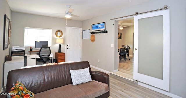 office space with baseboards, a ceiling fan, light wood finished floors, and a barn door
