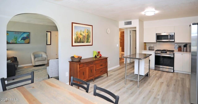 kitchen featuring visible vents, appliances with stainless steel finishes, arched walkways, light wood finished floors, and white cabinetry