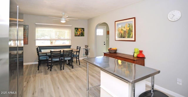 dining area with baseboards, arched walkways, a ceiling fan, and light wood-style flooring