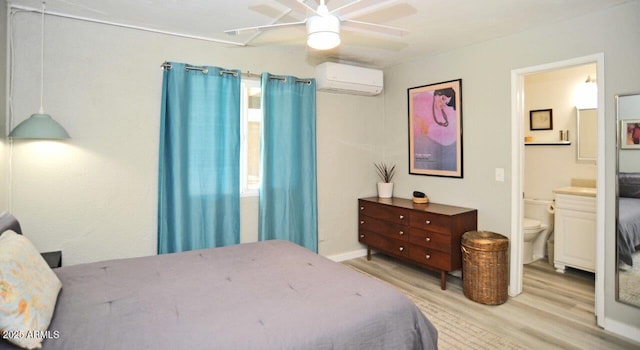 bedroom featuring an AC wall unit, a ceiling fan, connected bathroom, and light wood-type flooring