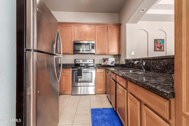 kitchen featuring light tile patterned flooring, sink, stainless steel appliances, and dark stone countertops