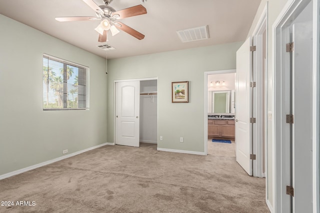 unfurnished bedroom featuring ensuite bathroom, ceiling fan, light colored carpet, and a closet