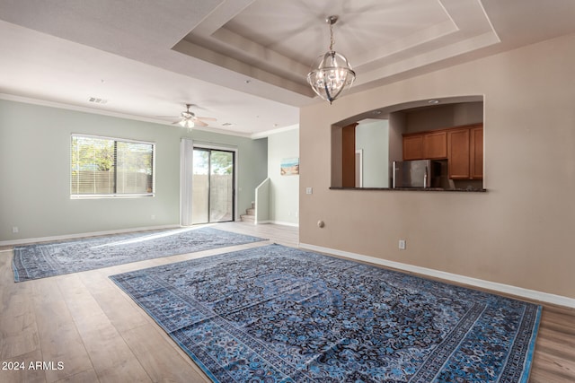 interior space with a raised ceiling, ceiling fan with notable chandelier, light hardwood / wood-style flooring, and crown molding