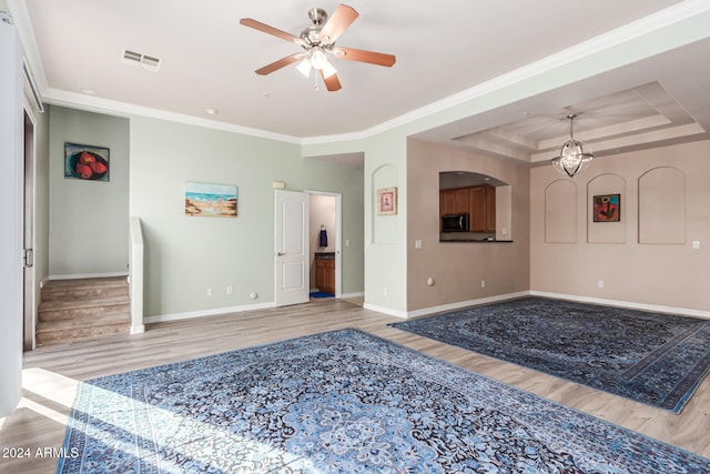 unfurnished living room featuring ceiling fan, light wood-type flooring, crown molding, and a tray ceiling