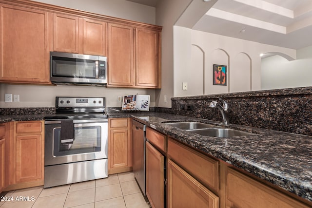 kitchen with dark stone counters, a raised ceiling, sink, light tile patterned floors, and stainless steel appliances