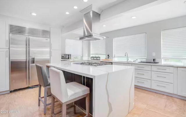 kitchen featuring appliances with stainless steel finishes, white cabinetry, a kitchen island, island exhaust hood, and a kitchen bar