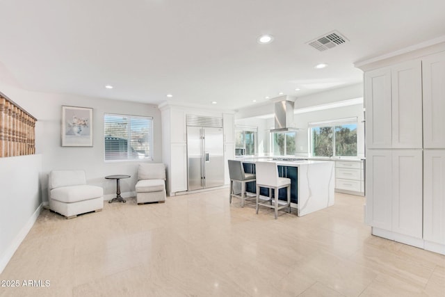 interior space with white cabinetry, island exhaust hood, built in refrigerator, and a kitchen breakfast bar