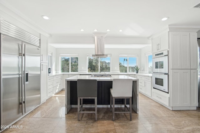 kitchen featuring island exhaust hood, appliances with stainless steel finishes, a breakfast bar, and white cabinets