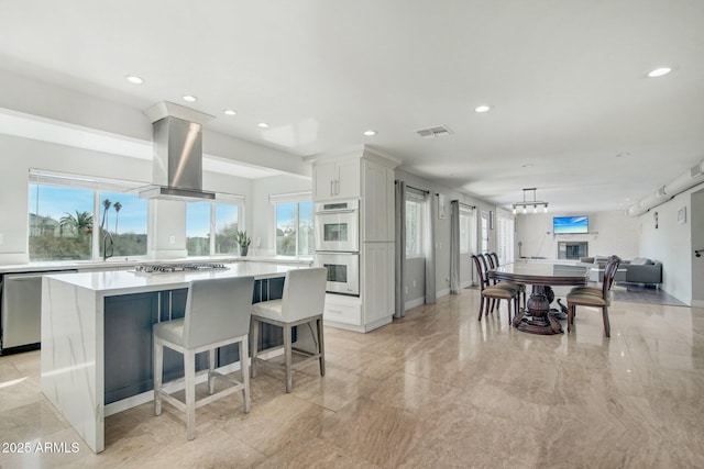 kitchen with appliances with stainless steel finishes, a center island, white cabinets, and island exhaust hood