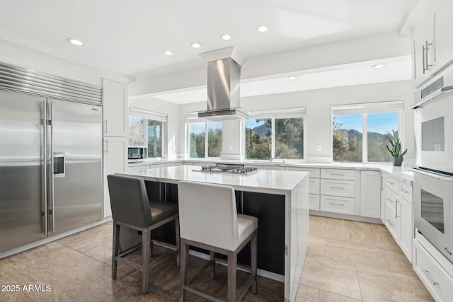 kitchen featuring a breakfast bar area, island range hood, a center island, appliances with stainless steel finishes, and white cabinets