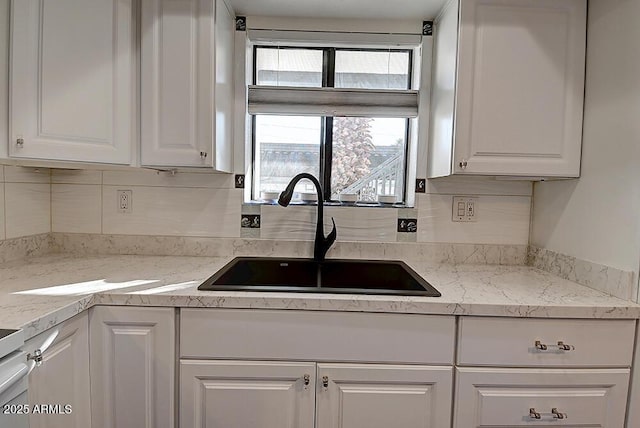 kitchen with tasteful backsplash, light stone countertops, sink, and white cabinets