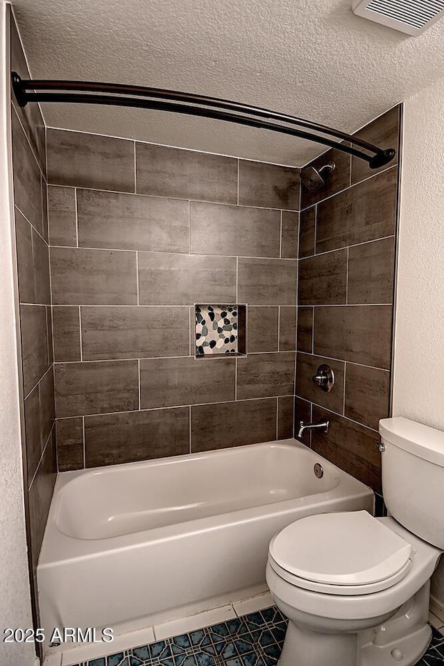 bathroom featuring tiled shower / bath, tile patterned floors, toilet, and a textured ceiling