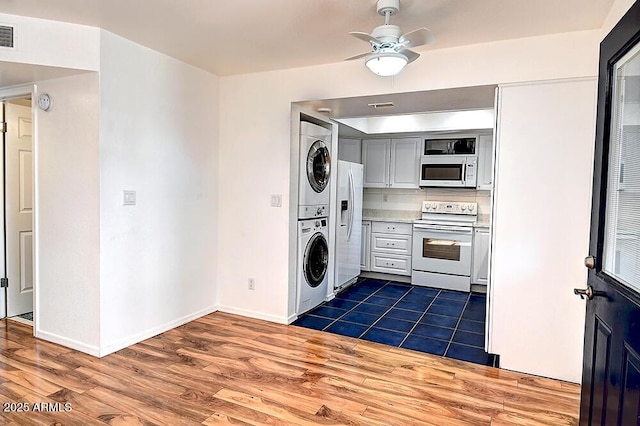 kitchen featuring dark hardwood / wood-style flooring, white appliances, ceiling fan, and stacked washing maching and dryer