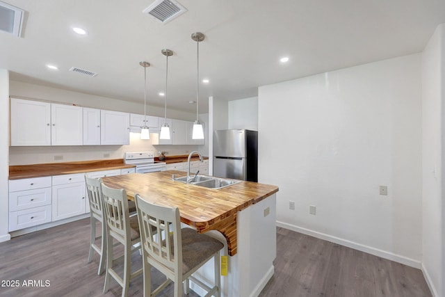 kitchen with visible vents, electric stove, a sink, freestanding refrigerator, and butcher block counters