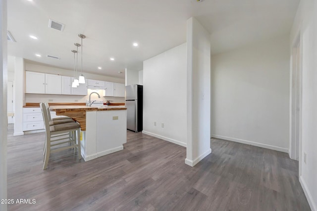 kitchen with visible vents, freestanding refrigerator, white cabinets, wood counters, and a sink