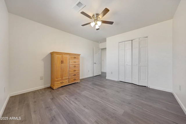 unfurnished bedroom featuring a ceiling fan, wood finished floors, visible vents, baseboards, and a closet