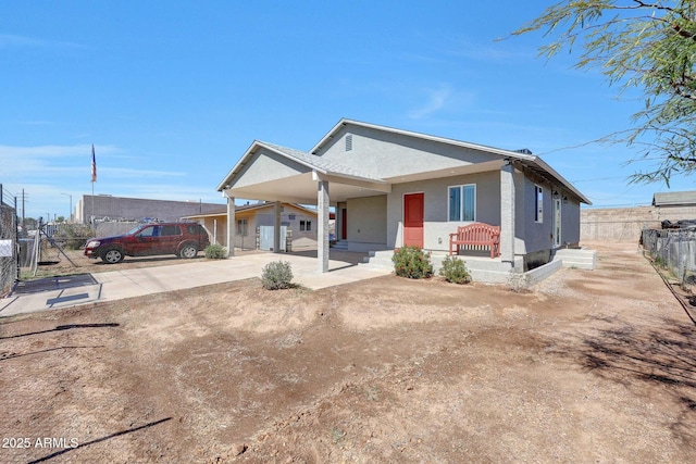 bungalow-style house with stucco siding, an attached carport, driveway, and fence