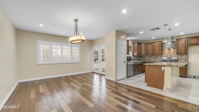 kitchen with light wood finished floors, wall chimney range hood, visible vents, decorative backsplash, and appliances with stainless steel finishes