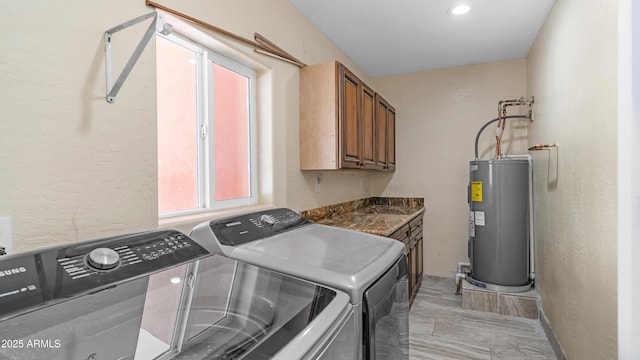 washroom featuring a textured wall, water heater, washer and clothes dryer, and cabinet space