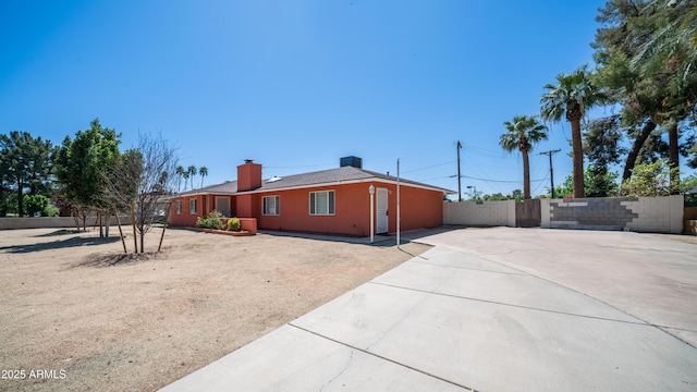 view of side of property featuring concrete driveway, fence, and a chimney