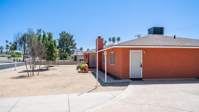 view of side of property featuring a chimney, roof with shingles, cooling unit, and stucco siding