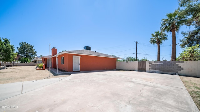 view of side of home featuring stucco siding, a patio, a chimney, and fence