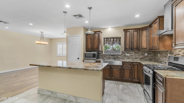 kitchen featuring a sink, tasteful backsplash, wall chimney range hood, a kitchen island, and appliances with stainless steel finishes