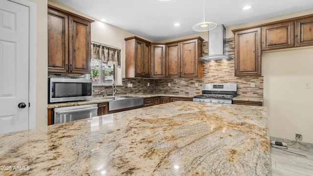 kitchen featuring wall chimney exhaust hood, a sink, tasteful backsplash, light stone counters, and appliances with stainless steel finishes