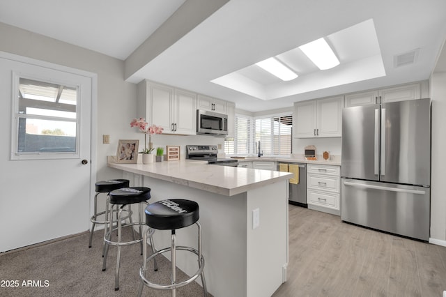 kitchen featuring appliances with stainless steel finishes, a breakfast bar, kitchen peninsula, white cabinets, and a tray ceiling