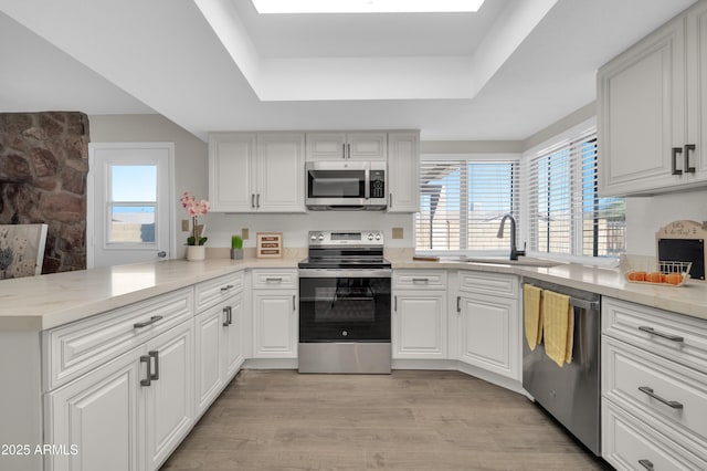 kitchen with a raised ceiling, sink, white cabinets, kitchen peninsula, and stainless steel appliances