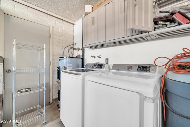 laundry area with brick wall, water heater, cabinets, washing machine and clothes dryer, and a textured ceiling