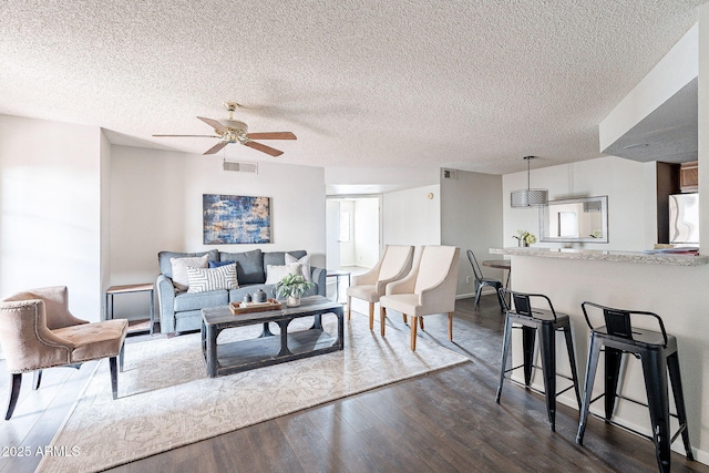 living area with ceiling fan, dark wood-style flooring, a textured ceiling, and visible vents