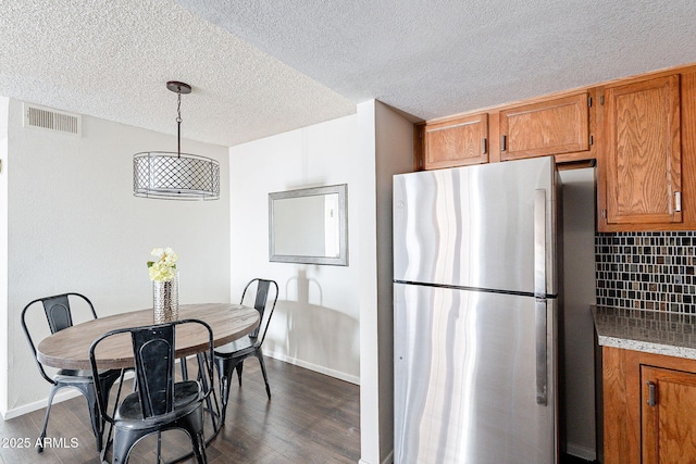 kitchen featuring visible vents, backsplash, freestanding refrigerator, and brown cabinets