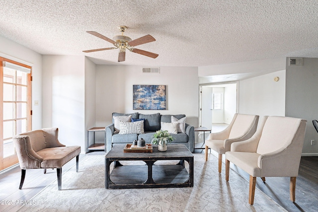 living area with a textured ceiling, wood finished floors, visible vents, and a ceiling fan