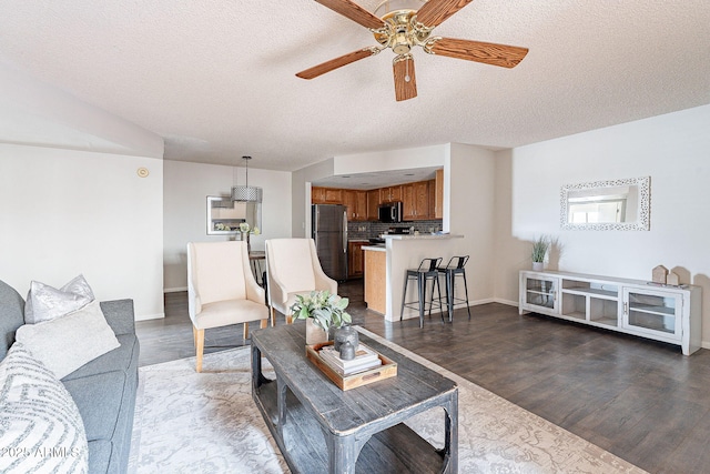 living room featuring dark wood-type flooring, ceiling fan, a textured ceiling, and baseboards