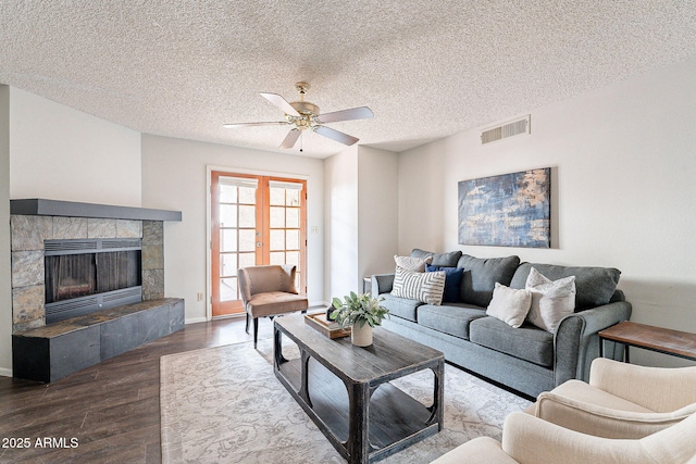 living room featuring a textured ceiling, a tile fireplace, wood finished floors, visible vents, and french doors