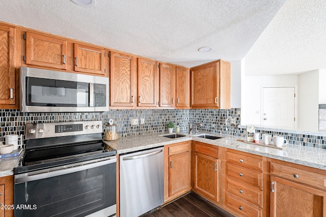 kitchen featuring dark wood-style floors, a sink, light stone countertops, stainless steel appliances, and backsplash