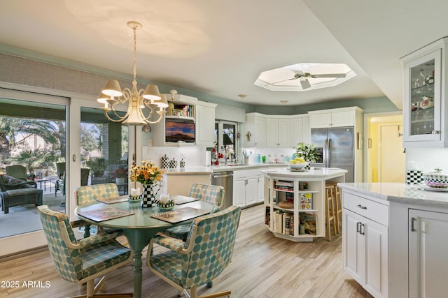 dining room with ceiling fan with notable chandelier, a skylight, light hardwood / wood-style floors, and sink