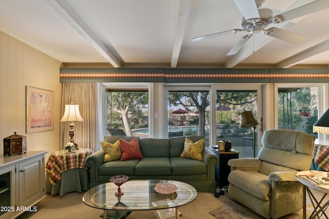 living room featuring ceiling fan, carpet flooring, a wealth of natural light, and beamed ceiling