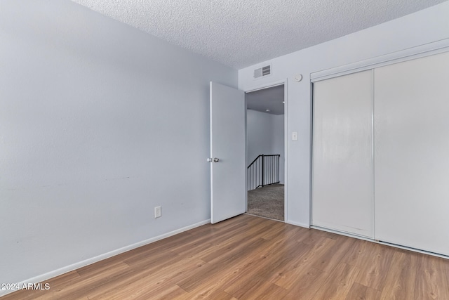 unfurnished bedroom featuring a closet, a textured ceiling, and light wood-type flooring