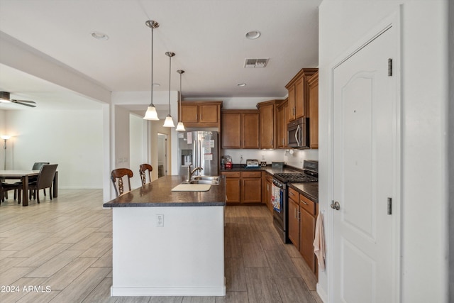 kitchen with hanging light fixtures, appliances with stainless steel finishes, light hardwood / wood-style floors, sink, and a kitchen island with sink