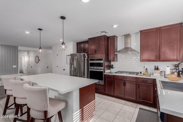 kitchen featuring appliances with stainless steel finishes, decorative light fixtures, light tile patterned floors, decorative backsplash, and wall chimney exhaust hood