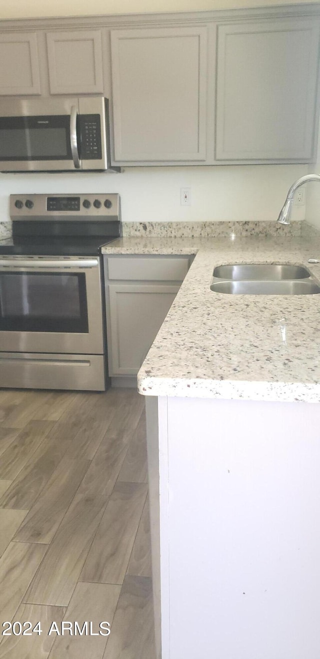 kitchen with appliances with stainless steel finishes, gray cabinetry, dark wood-type flooring, light stone countertops, and sink