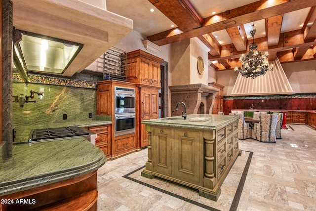 kitchen with sink, beam ceiling, a chandelier, a kitchen island with sink, and double oven