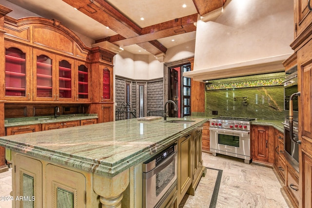 kitchen with light stone counters, appliances with stainless steel finishes, beam ceiling, sink, and a spacious island